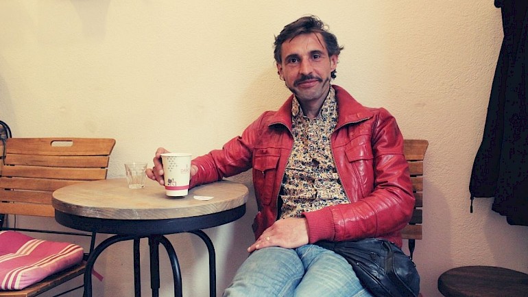 Tom Vogel sitzt in roter Jacke beim Kaffee